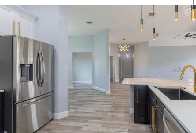 kitchen featuring stainless steel appliances, hanging light fixtures, sink, and light hardwood / wood-style flooring