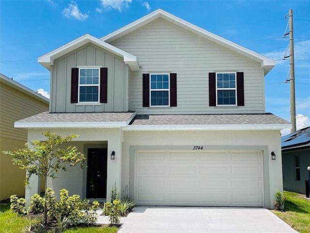 traditional home with board and batten siding, an attached garage, driveway, and roof with shingles