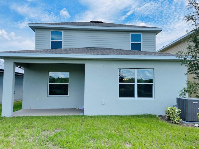 back of house featuring roof with shingles, a patio, a yard, and central AC