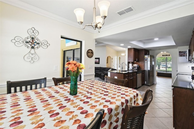 tiled dining room featuring an inviting chandelier, crown molding, sink, and a raised ceiling