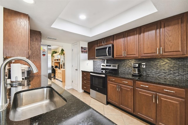 kitchen with appliances with stainless steel finishes, dark stone countertops, a tray ceiling, and sink