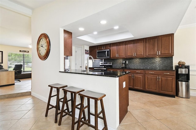 kitchen with light tile patterned flooring, kitchen peninsula, decorative backsplash, appliances with stainless steel finishes, and dark stone countertops