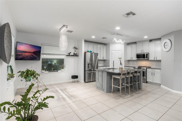 kitchen featuring stainless steel appliances, decorative backsplash, sink, a kitchen island with sink, and a breakfast bar