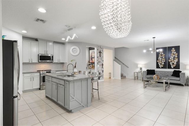 kitchen with sink, a kitchen island with sink, a breakfast bar, appliances with stainless steel finishes, and decorative light fixtures