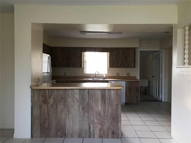 kitchen with dark brown cabinets, kitchen peninsula, appliances with stainless steel finishes, and light tile patterned floors