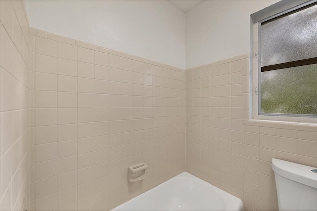 bathroom featuring tile walls, a bathing tub, and toilet