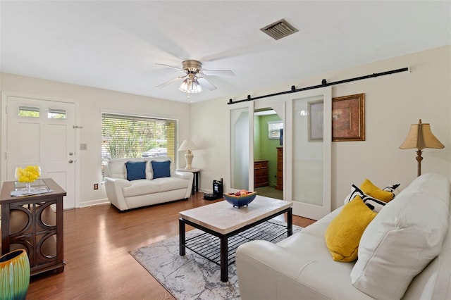 living room featuring wood-type flooring, ceiling fan, and a barn door