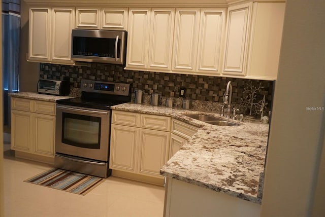 kitchen with appliances with stainless steel finishes, cream cabinetry, and sink