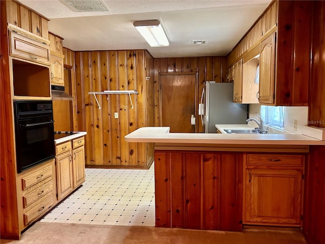 kitchen featuring wood walls, kitchen peninsula, stainless steel refrigerator, and sink