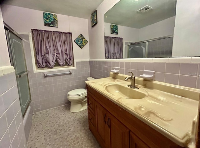 full bathroom with tile walls, tile patterned flooring, combined bath / shower with glass door, vanity, and toilet