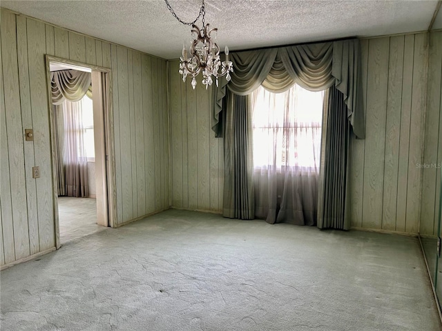 spare room with a notable chandelier, wood walls, a textured ceiling, and light carpet