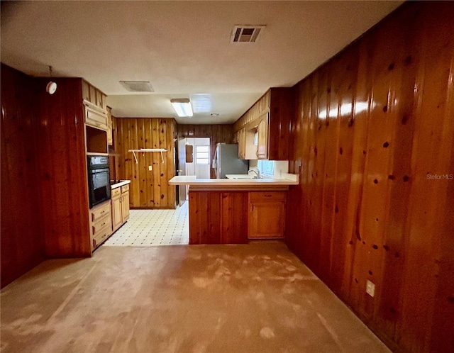 kitchen featuring stainless steel refrigerator, kitchen peninsula, wood walls, black oven, and light colored carpet