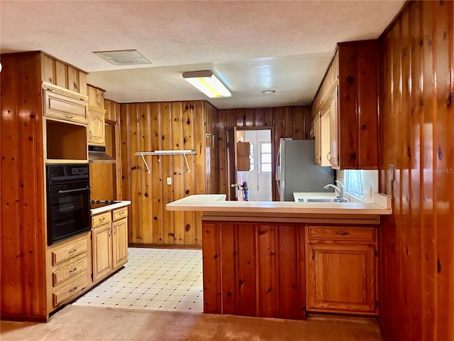 kitchen featuring wood walls, black oven, stainless steel fridge, and kitchen peninsula