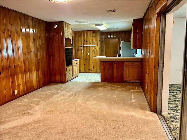 kitchen with wood walls, kitchen peninsula, stainless steel refrigerator, light carpet, and black oven