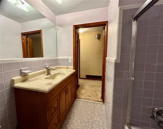 bathroom with tile walls, tile patterned flooring, vanity, and a tile shower