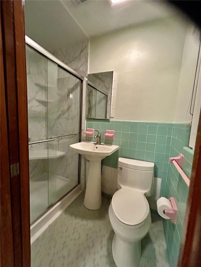 bathroom with tile walls, toilet, and an enclosed shower