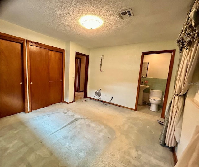 unfurnished bedroom with light carpet, ensuite bath, and a textured ceiling