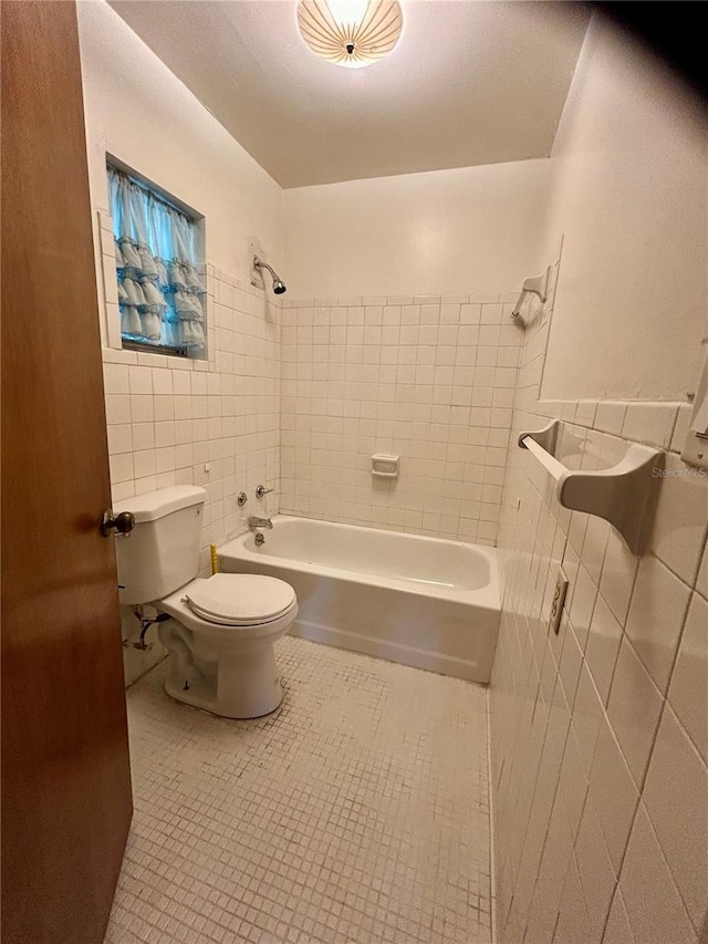 bathroom featuring tile walls, tiled shower / bath combo, and toilet