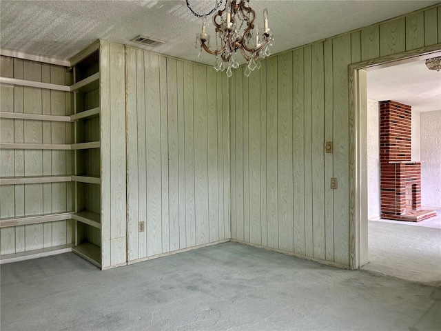 interior space with carpet floors, a fireplace, a textured ceiling, wooden walls, and a notable chandelier