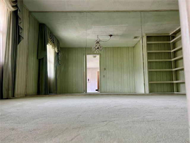 empty room featuring built in shelves, carpet flooring, a textured ceiling, and a chandelier