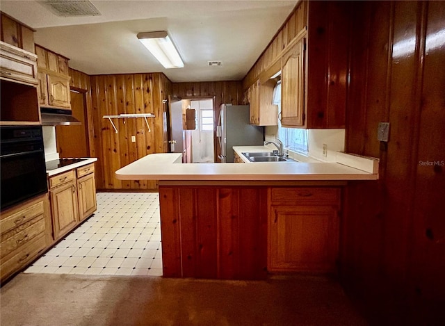 kitchen featuring wood walls, sink, kitchen peninsula, oven, and stainless steel refrigerator