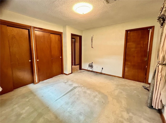 unfurnished bedroom featuring a textured ceiling, two closets, and light carpet