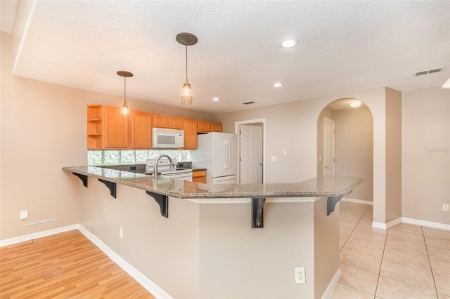 kitchen with a kitchen breakfast bar, decorative backsplash, white appliances, kitchen peninsula, and pendant lighting