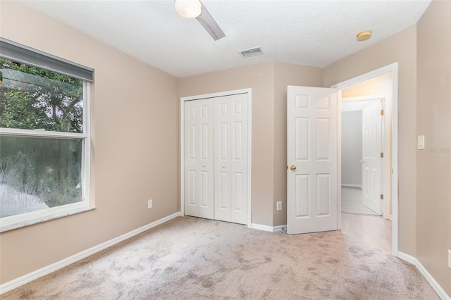 unfurnished bedroom with ceiling fan, a textured ceiling, a closet, and light carpet