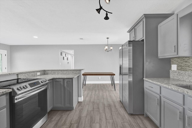 kitchen featuring pendant lighting, appliances with stainless steel finishes, light hardwood / wood-style floors, gray cabinets, and light stone counters