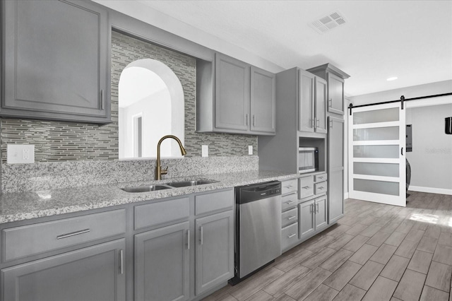 kitchen with gray cabinets, sink, a barn door, and stainless steel dishwasher