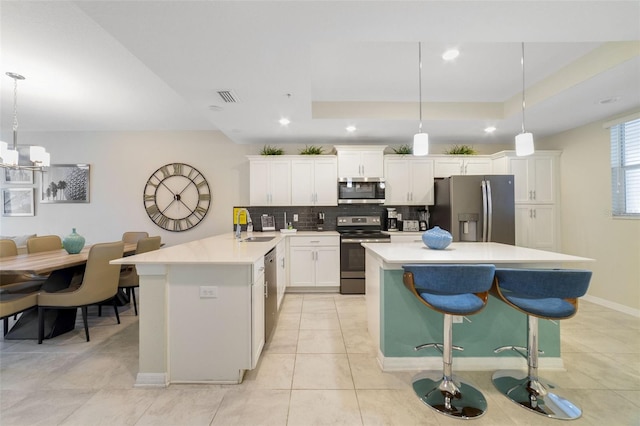 kitchen featuring pendant lighting, white cabinets, tasteful backsplash, a kitchen breakfast bar, and stainless steel appliances