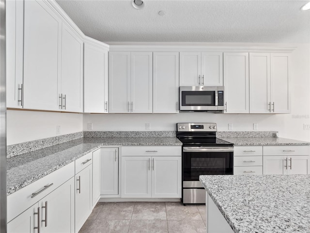 kitchen featuring light stone counters, white cabinets, light tile patterned floors, stainless steel appliances, and a textured ceiling