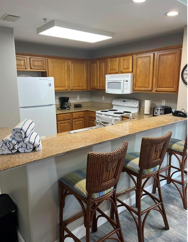 kitchen featuring a kitchen breakfast bar, light wood-type flooring, white appliances, and kitchen peninsula