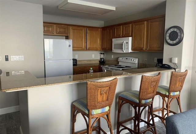 kitchen with a kitchen bar, kitchen peninsula, white appliances, and stone countertops