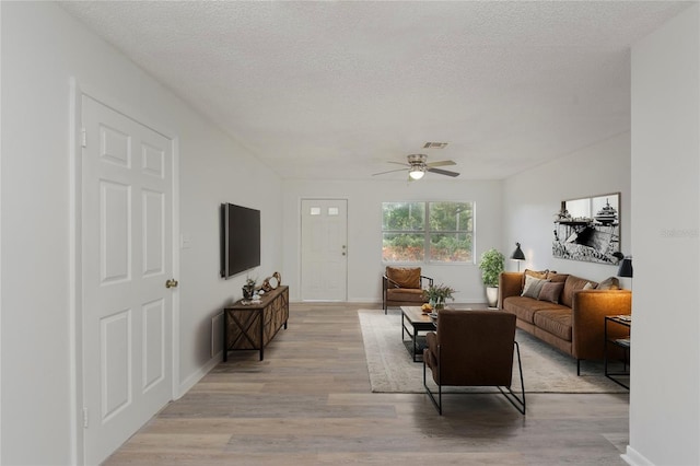 living room featuring light hardwood / wood-style flooring, ceiling fan, and a textured ceiling