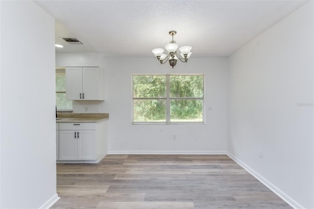 unfurnished dining area featuring light hardwood / wood-style flooring, a chandelier, and a textured ceiling