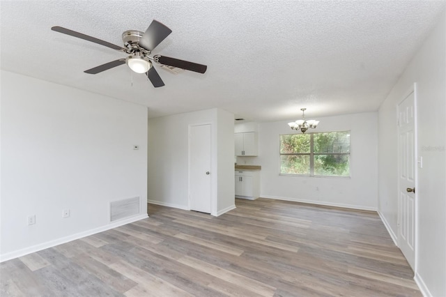 unfurnished living room with light wood-type flooring, ceiling fan with notable chandelier, and a textured ceiling