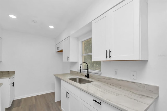 kitchen featuring white cabinets, light stone counters, light wood-type flooring, and sink