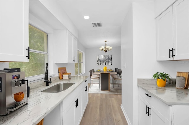 kitchen featuring light wood-type flooring, a notable chandelier, sink, and white cabinets