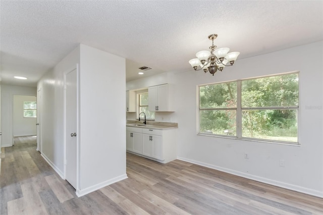 kitchen with sink, decorative light fixtures, a chandelier, white cabinetry, and light wood-type flooring