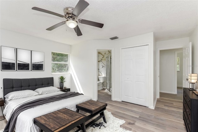 bedroom with light wood-type flooring, a closet, a textured ceiling, ensuite bathroom, and ceiling fan