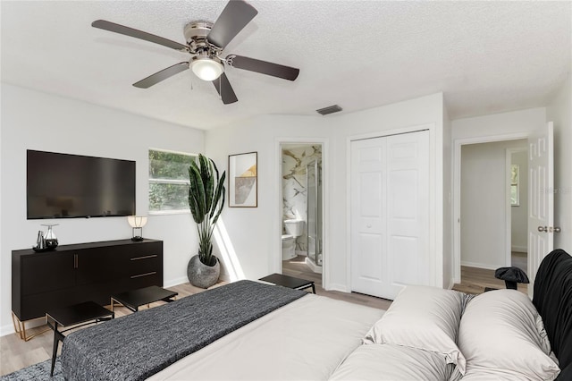 bedroom with light wood-type flooring, a textured ceiling, ensuite bath, and ceiling fan