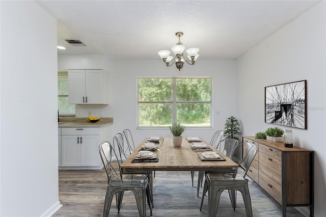 dining area with a textured ceiling, an inviting chandelier, and hardwood / wood-style flooring