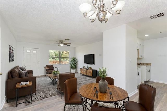 dining area featuring ceiling fan with notable chandelier, light wood-type flooring, and a textured ceiling