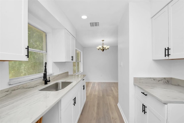 kitchen featuring white cabinetry, light hardwood / wood-style floors, decorative light fixtures, and sink