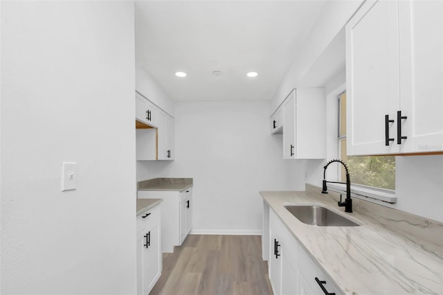 kitchen featuring light wood-type flooring, white cabinetry, light stone counters, and sink