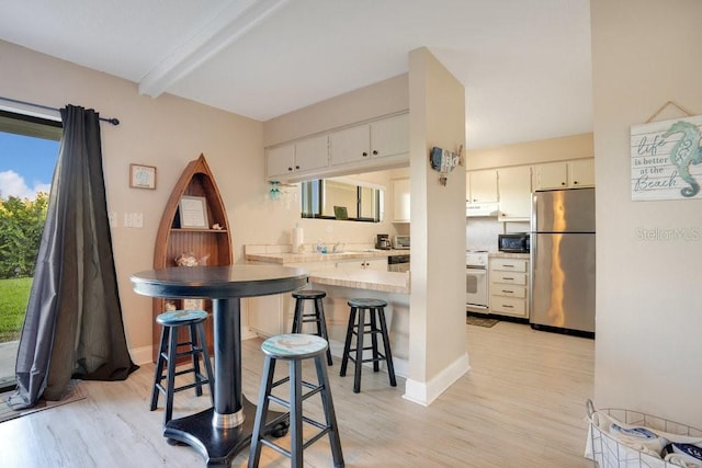 kitchen featuring light wood-type flooring, a breakfast bar area, white cabinets, kitchen peninsula, and stainless steel fridge