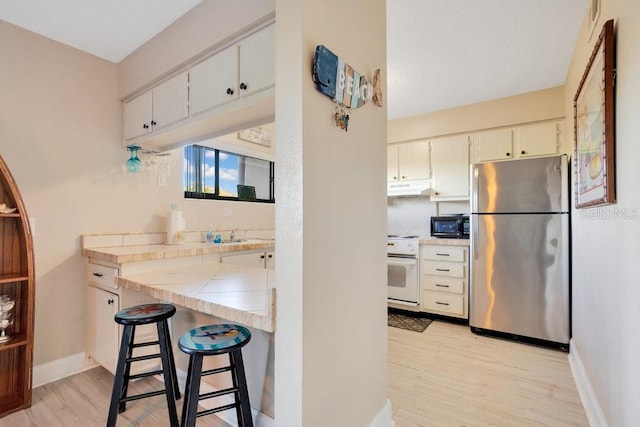 3150 N Atlantic Ave Unit 3-550, Cocoa Beach, FL 32931 - kitchen with freestanding refrigerator, under cabinet range hood, black microwave, stove, and light wood-style flooring