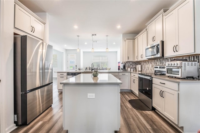 kitchen with kitchen peninsula, stainless steel appliances, decorative light fixtures, hardwood / wood-style floors, and a kitchen island