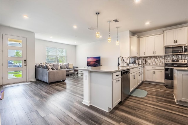 kitchen with kitchen peninsula, stainless steel appliances, dark wood-type flooring, white cabinetry, and hanging light fixtures